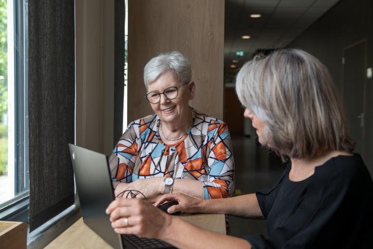 Behandelaar kijkt met senior vrouw naar laptop